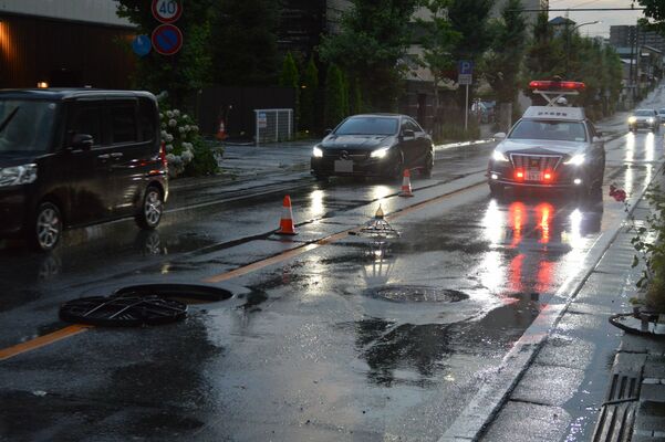 大雨の影響でマンホールがずれたままの道路。警察官が交通整理に当たった＝11日午後６時55分、宇都宮市昭和１丁目（画像は一部を修正しています）