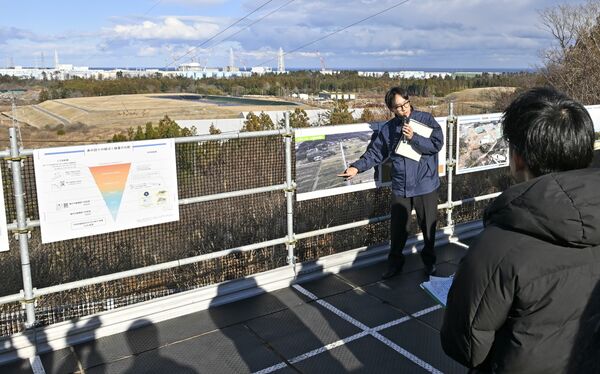 中間貯蔵施設を見渡せる高台で記者（右手前）に説明する環境省職員。奥には福島第１原発も見える＝８日午後１時50分、福島県大熊町、広瀬華撮影