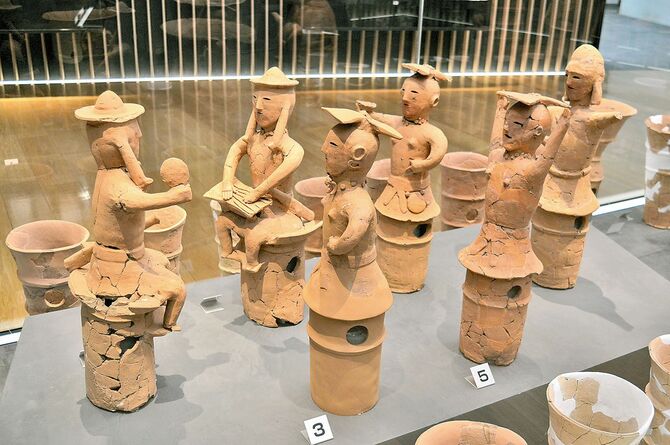 軍配を手に椅子に座る男子（左）と琴を弾く男子（左奥２番目）は帽子を被り、足まで表現され、巫女は省略されている「飯塚31号古墳出土人物埴輪」。摩利支天・琵琶塚古墳資料館（小山）所蔵