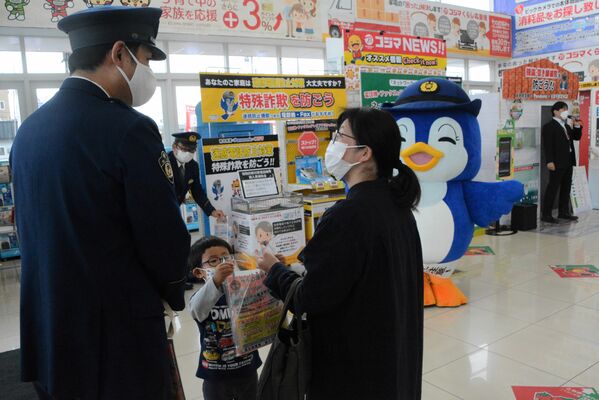 防犯機能付き電話機を説明する県警の警察官（左）＝13日午前、宇都宮市今泉町