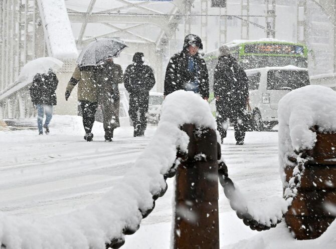  雪の日に傘を差す人、差さない人が行き交う盛岡市の開運橋周辺