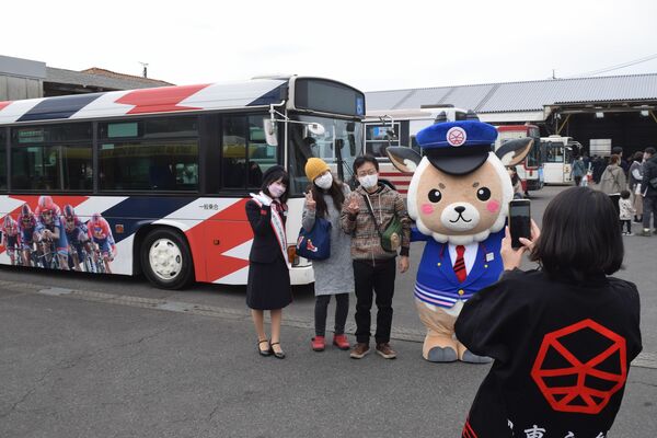 展示されたバスを背景に、マスコットキャラクター「かもーるくん」と記念撮影する来場者＝20日午前、宇都宮市中一の沢町