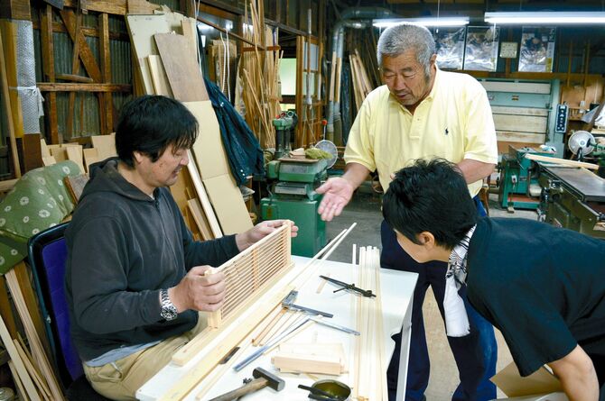 吉原木芸の社長、吉原幸二さん（右上）から制作中の鹿沼組子について説明を聞くリポーターＫ（右下）