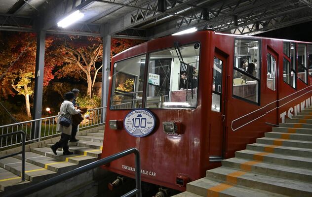 ライトアップされた紅葉の下、開業１００周年のヘッドマークを備え運行するケーブルカー