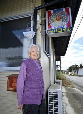 「理容ハコイシ」の看板前に立つ箱石さん。その笑顔は、人生の荒波を乗り越えてきたたくましさの表れだ＝那珂川町谷川、杉浦崇仁撮影