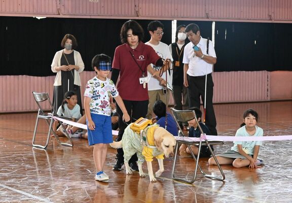 アイマスクを着用して盲導犬との歩行体験をする児童
