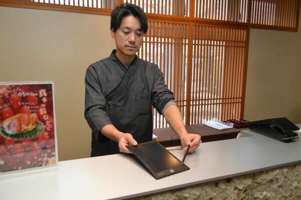 電子メモパッドを手にする船曵社長。聴覚障害者を接客する際に使っている＝３月、日光市川治温泉川治