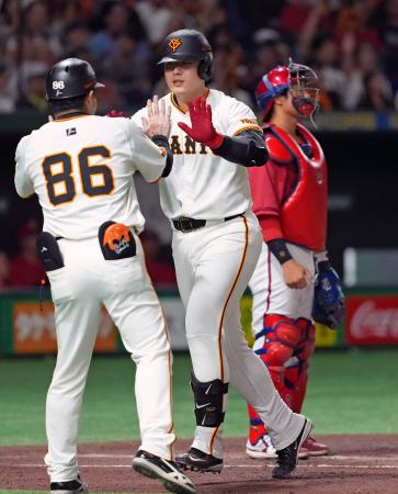 2回、先制ソロを放ちコーチとタッチを交わす巨人・岡本。広島の捕手石原=東京ドーム