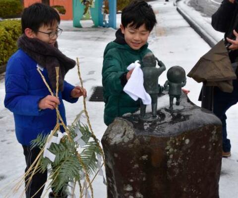 　「水木しげるロード」にある妖怪などのブロンズ像にしめ飾りを取り付ける子どもたち＝２６日、鳥取県境港市