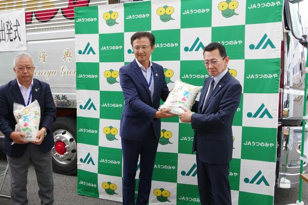 加藤社長（右）にコメを引き渡す佐藤組合長（中央）＝28日午前、宇都宮市