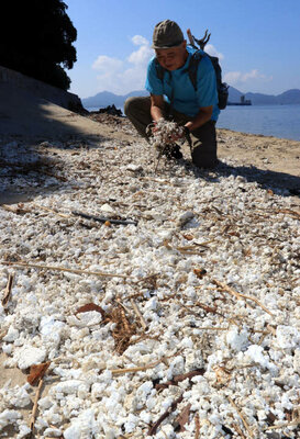 宇品島の海岸に打ち上げられたフロートの破片を手にする藤原さん（広島市南区）