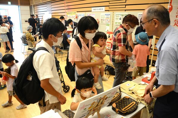 高級ブランド品の本物と偽物を見比べる親子連れ＝14日午前、宇都宮市雀宮町