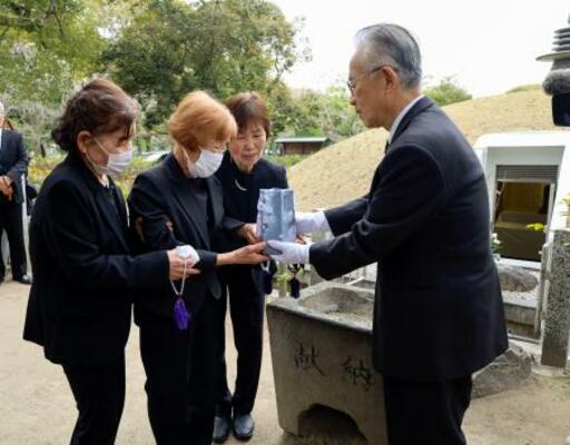 13歳で被爆して亡くなった梶山初枝さんの遺骨を受け取る妹の美智子さん(左から2人目)。右奥は原爆供養塔=22日午前、広島市の平和記念公園