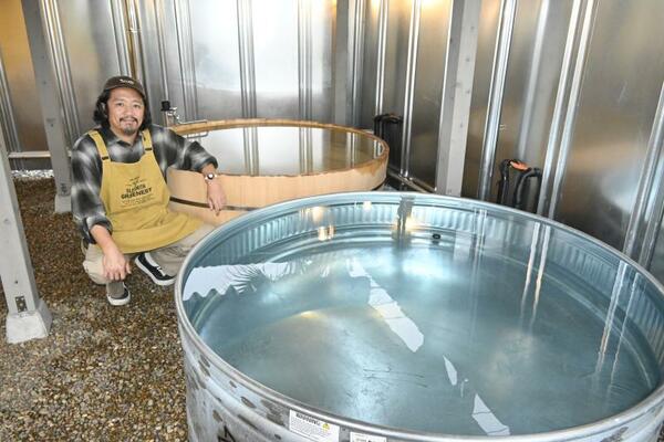 ワロウズを経営する大倉さん。町の魅力である尚仁沢湧水を使った水風呂（手前）と、町の丸木風呂職人が作った風呂桶を楽しめる温水風呂