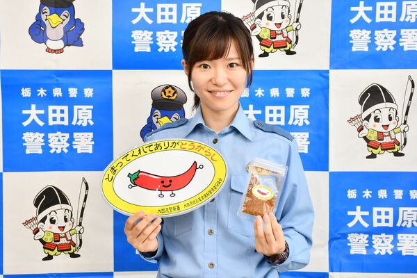 トウガラシをモチーフにした啓発用のステッカーを持つ石川警部補