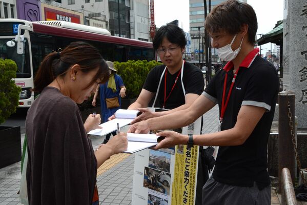 署名に協力する通行人（左端）＝18日午後、宇都宮市馬場通り４丁目
