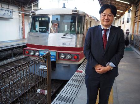 　富山地鉄１６０１０形の脇に立つ筆者。西嶋伸一さんが撮ってくださった＝２５年１０月２３日、富山市