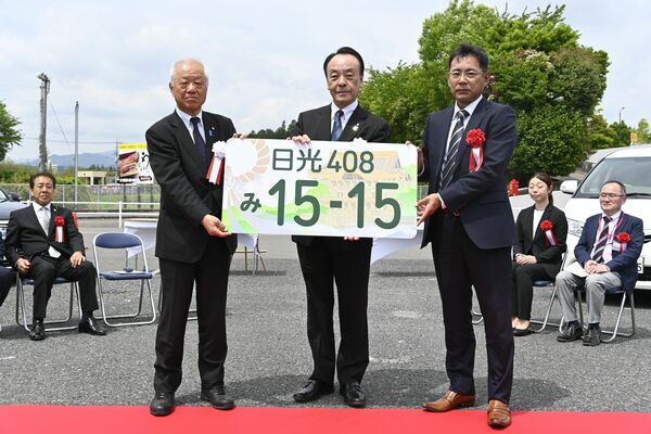 図柄入りナンバーの交付を受ける関教育長（中央）と塩谷町の見形町長（左）＝15日午前、日光市豊田
