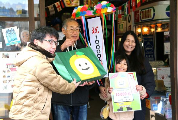 １万人目の来場者となり、滝田課長（左）から記念品を受け取る鈴木さん一家