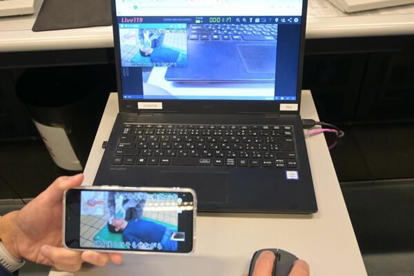 通報者のスマホ(手前)での撮影映像が映し出された指令員のパソコン画面のイメージ(画像は一部加工しています)