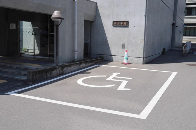 幅が広い車いすマークの駐車区画。京都府が運用する制度へ協力する場合、その旨も掲示（奥のコーン）している＝京都市上京区・府庁