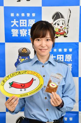 トウガラシをモチーフにした啓発用のステッカーを持つ石川警部補
