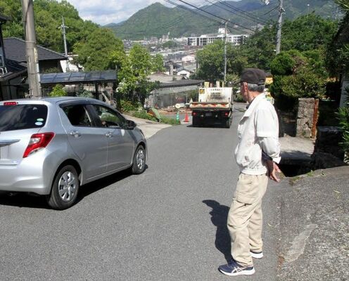 私道を通る車を確認する世良会長。奥に見える建物が市立北部医療センター安佐市民病院
