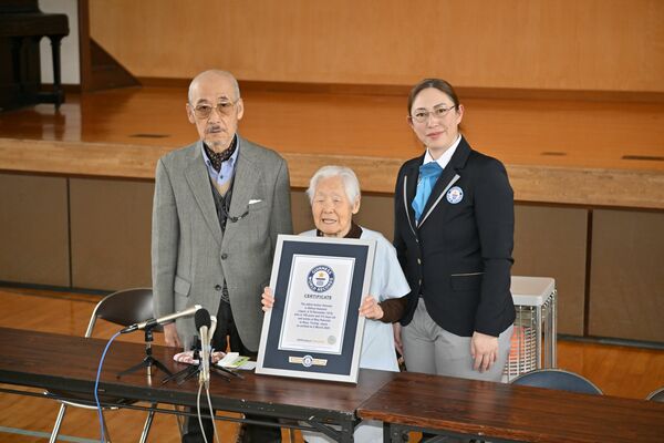 ギネス登録証を手に笑顔を見せる箱石シツイさん（中央）。左は長男の英政さん＝5日午前10時35分、那珂川町谷川