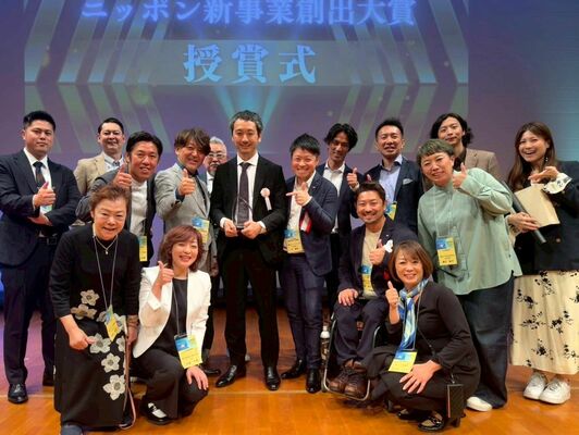 最優秀賞のクリスタルの盾を持つ「ＧＯＯＤ　ＮＥＷＳ」の宮本ＣＣＯ（中列左から４人目）と支援したとちぎニュービジネス協議会のメンバー＝23日午後、福岡市（とちぎニュービジネス協議会提供）