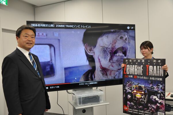 「ゾンビトレイン」のＰＲ動画とポスターを紹介する粉川市長（左）