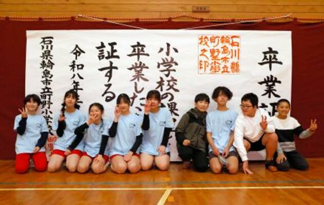 大きな紙でできた「卒業証書」の前で、記念写真に納まる川原脩伸さん(右端)ら=21日午後、石川県輪島市の町野小