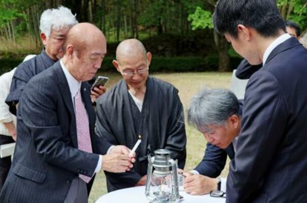 「平和の塔」から移された原爆の残り火を手にする佐々木雅弘さん(左)=20日午前、福岡県八女市
