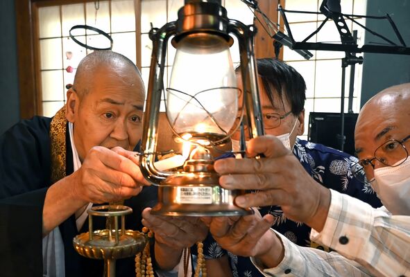 行進に使う小型ランプに残り火を移す人見住職(左)ら=4日午前10時10分、さくら市鹿子畑