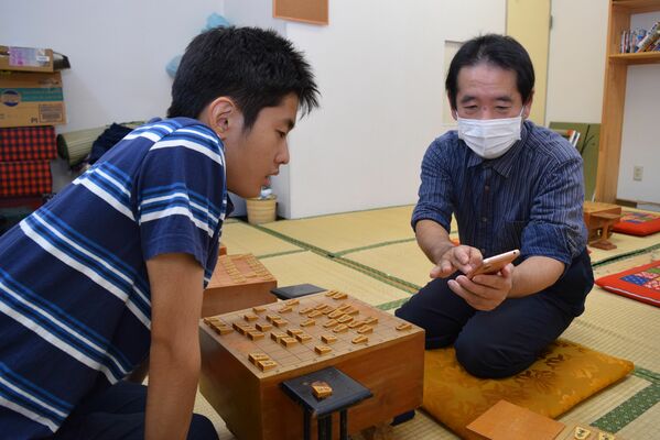 将棋を指しながらスマートフォンで王座戦の戦況を見つめる桐山さん（右）と生徒の二上さん＝11日午後８時30分、宇都宮市東宿郷６丁目