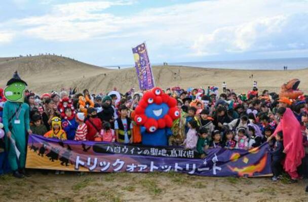 鳥取砂丘で開かれたハロウィーンパーティーに登場した「ミャクミャク」と記念撮影する参加者=26日午後、鳥取市
