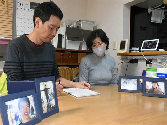 裁判を記録したノートを見つめる奥勝さん（左）と妻友子さん。手前の写真は長男公輝さん＝10月下旬、さくら市氏家