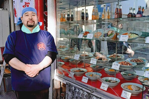 食品サンプルが並ぶ店頭に立つ仁瓶さん