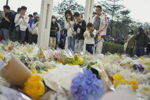 　火災現場の高層住宅群の近くで手を合わせる人たち＝２９日、香港北部・新界地区大埔