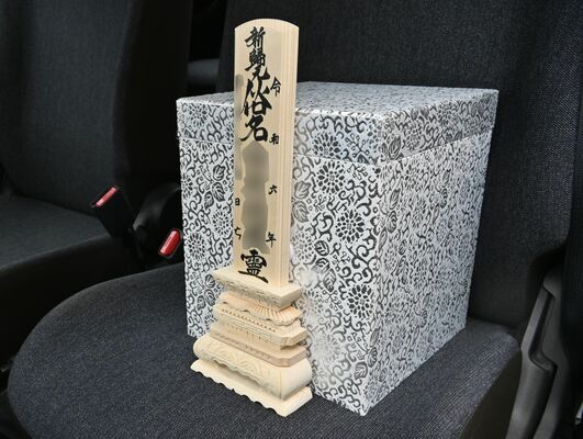 荼毘に付された女性の骨箱と位牌。三松会の車にそっと置かれた＝９日午後、群馬県館林市（写真は一部加工しています）