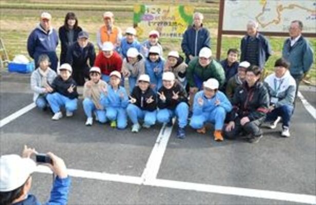 立てた看板を背に記念写真を撮る逆川小の児童や関係者たち