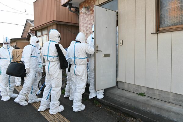 防護服を着て家宅捜索に入る捜査員＝15日午前10時、足利市内