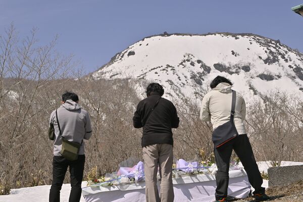 雪に覆われた事故現場を望む献花台で手を合わせる来訪者＝２７日午前１１時、那須町湯本