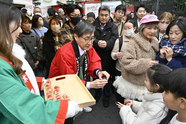 来場者にイチゴを手渡す若菜社長（中央）＝16日午後、東京都渋谷区