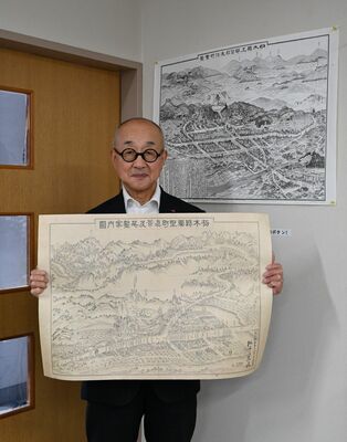 復刻した大正時代の粟野町の鳥瞰図を手にする阿部社長。右上は鹿沼町の鳥瞰図