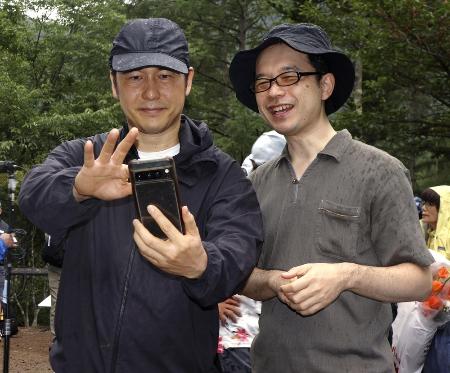 尾根に立つ「昇魂之碑」の前で母親とテレビ電話をつないだ山本昌由さん（右）と弟の康正さん＝８月１２日、群馬県上野村
