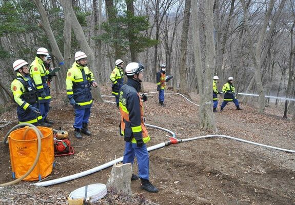 山林火災を想定した訓練で、山道をつないだホースを使って放水する消防団員ら
