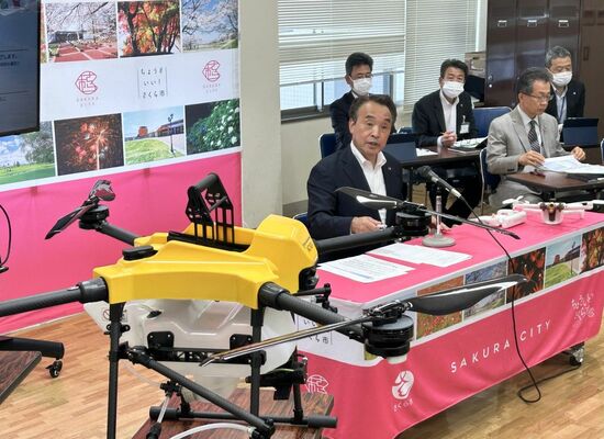大型ドローン（左）を前に会見する花塚市長