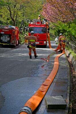 　岩手県大槌町の山林火災の現場付近でホースを回収する消防隊員＝３０日午前