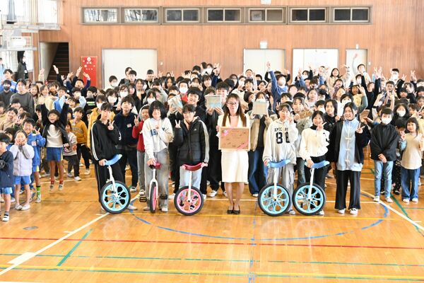 同校で行われた贈呈式で、メッセージボードを手にする小澤さん（中央）