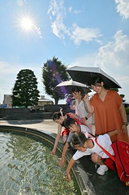 日傘を差しながら水場で涼を取る家族連れ＝26日午後３時25分、佐野市若松町、河野光吉撮影